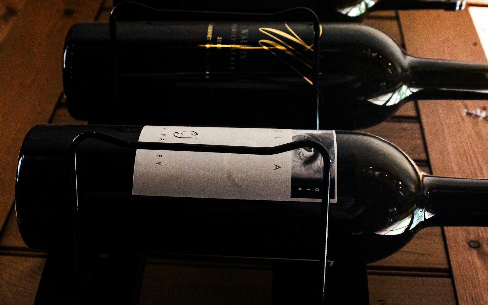 Bouteilles de vin couchées sur un casier en bois, dans la pénombre d’une cave.